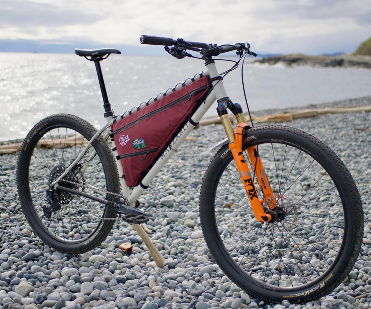 Burgundy frame bag fitted to a hardtail on a pebble beach