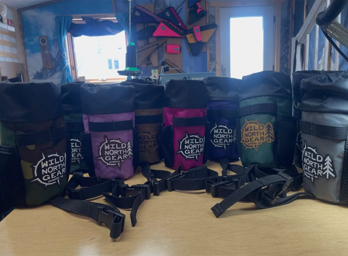 A row of finished bags with Wild North Gear patches on the workshop bench